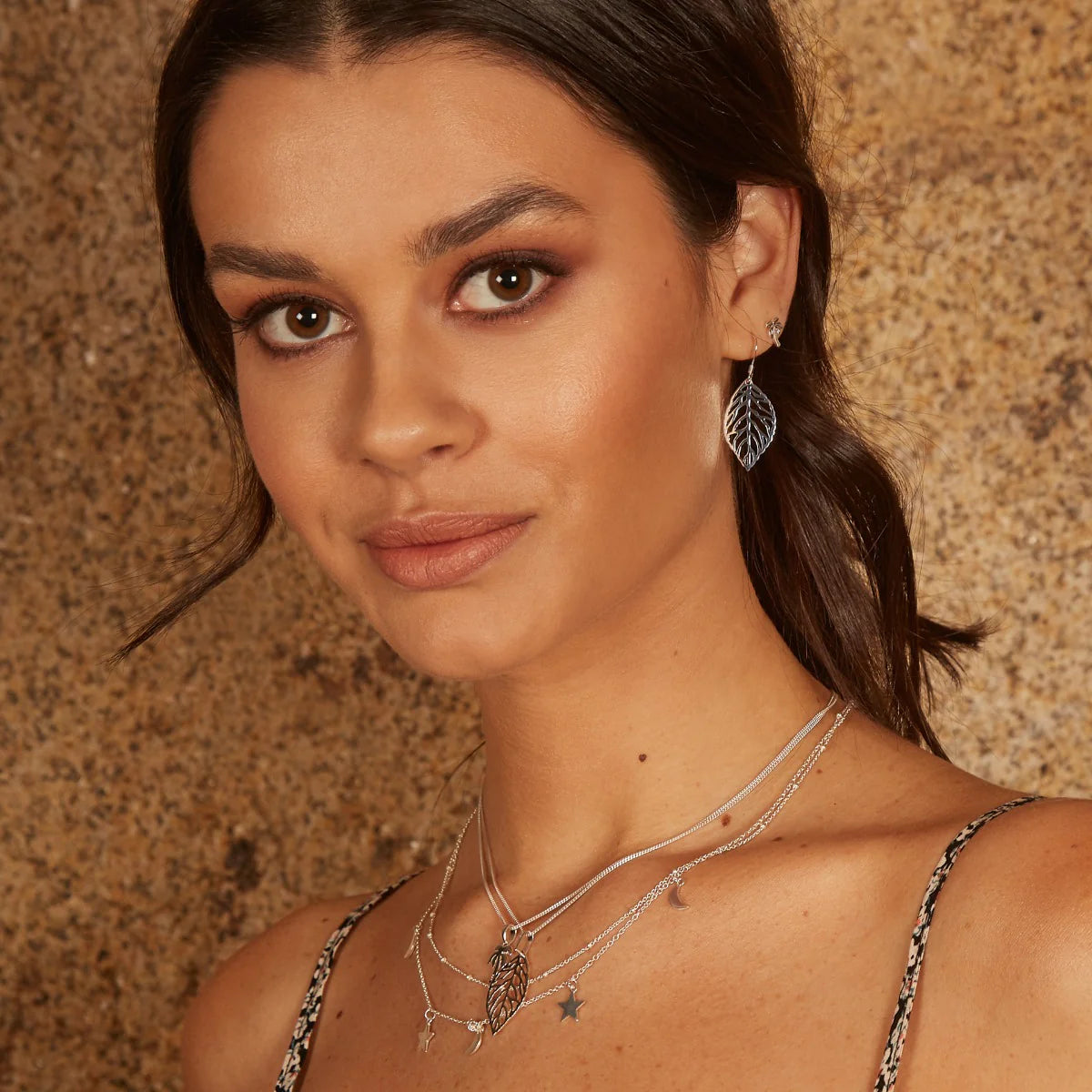 Woman wearing silver jewelry against a textured brown background