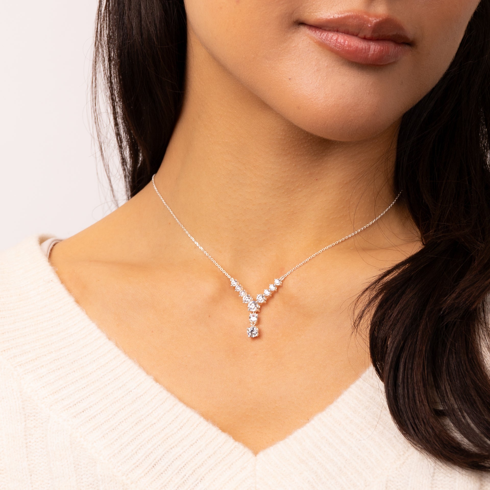 Woman wearing a delicate silver necklace with a small pendant on a plain background - presented by Alpha Bijoux