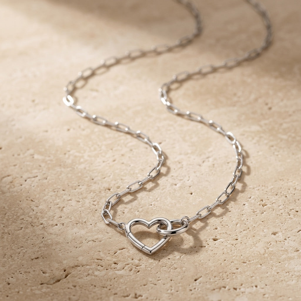 Silver heart-shaped necklace on a beige stone surface
