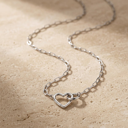 Silver heart-shaped necklace on a beige stone surface