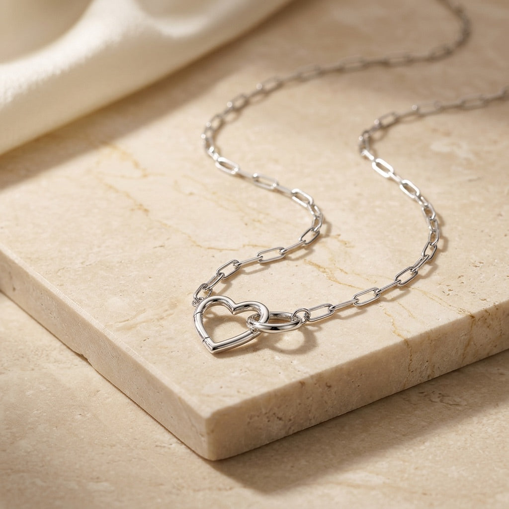 Silver chain necklace with heart design on a beige stone surface