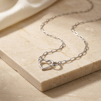 Silver chain necklace with heart design on a beige stone surface