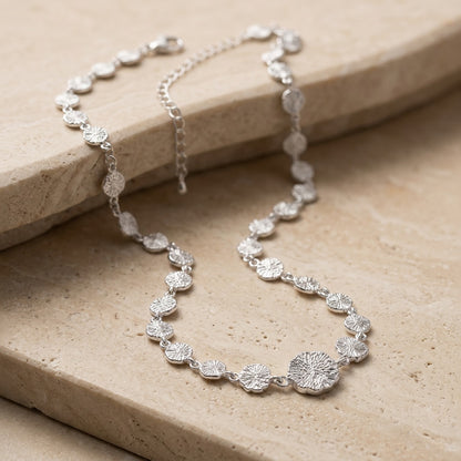 Silver necklace on a beige stone surface