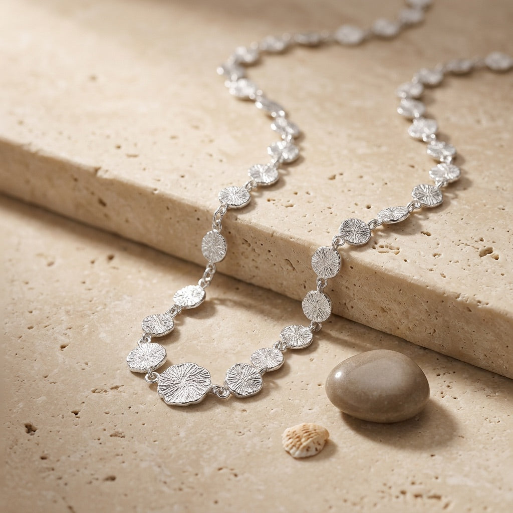 Silver necklace with floral designs on a beige stone surface