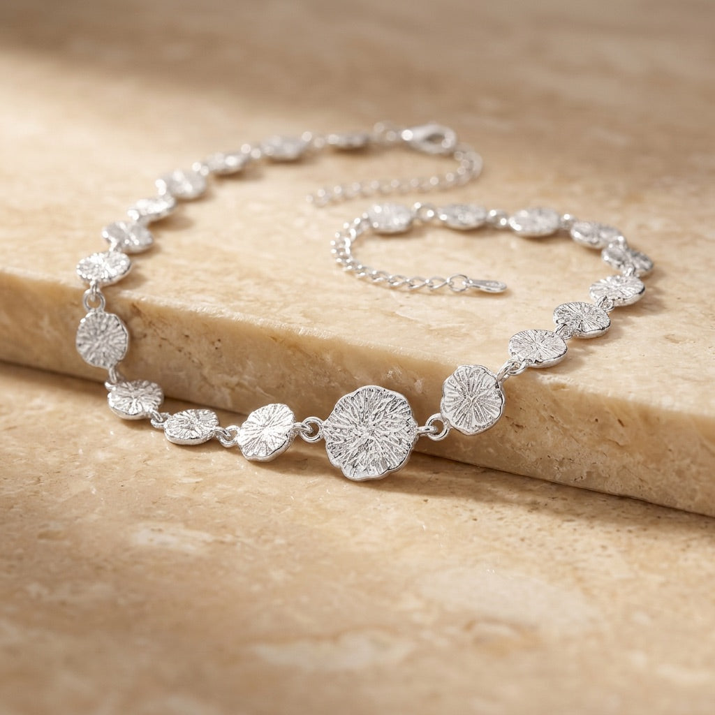 Silver bracelet with floral designs on a beige stone surface
