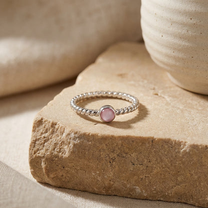 Silver ring with a pink gemstone on a beige stone surface