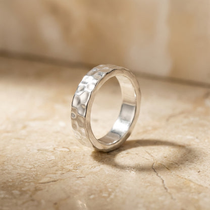 Silver ring with a textured band on a beige marble surface