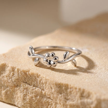 Silver ring with floral design on a beige stone surface