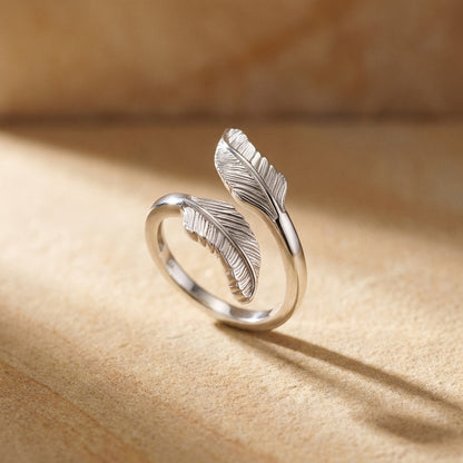 Silver feather-shaped ring on a beige surface