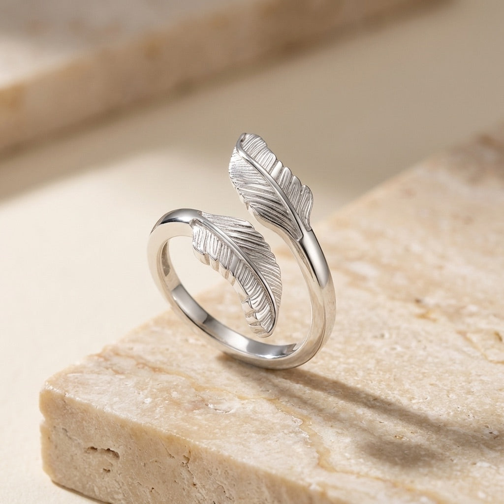 Silver feather-shaped ring on a beige stone surface