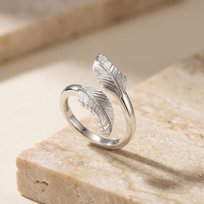 Silver feather-shaped ring on a beige stone surface