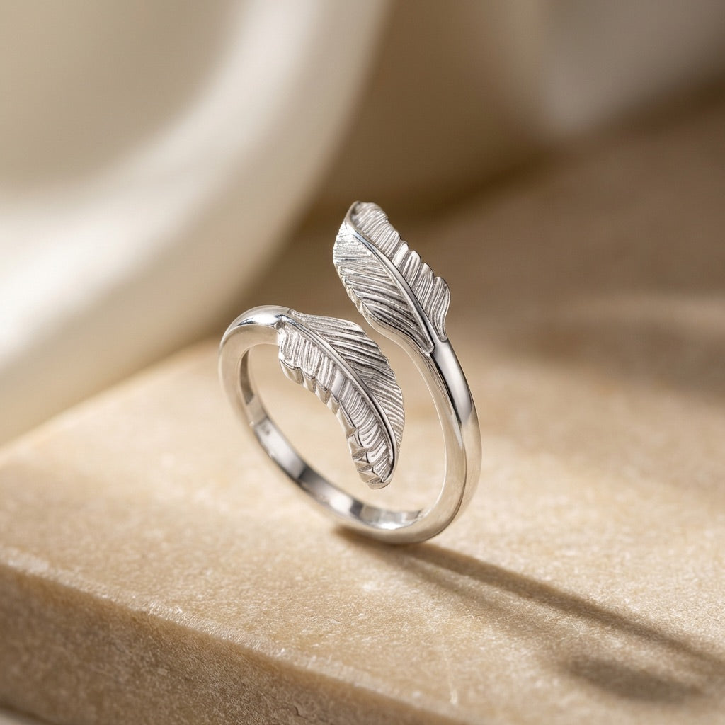 Silver feather-shaped ring on a beige surface