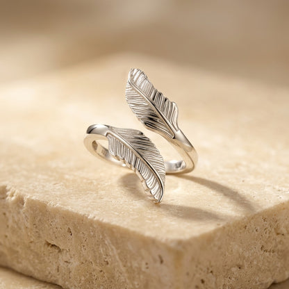 Silver feather-shaped ring on a beige stone surface