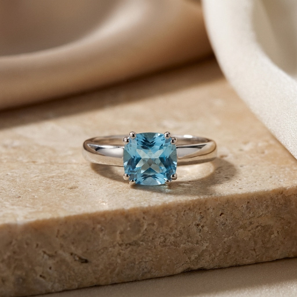 Silver ring with a blue gemstone on a beige stone surface