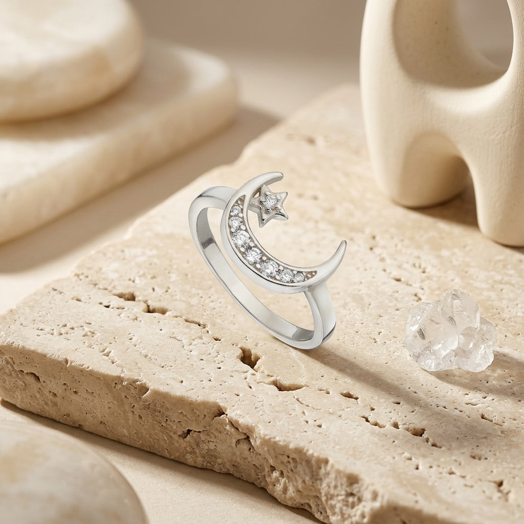 Silver ring with moon and star design on a textured beige surface