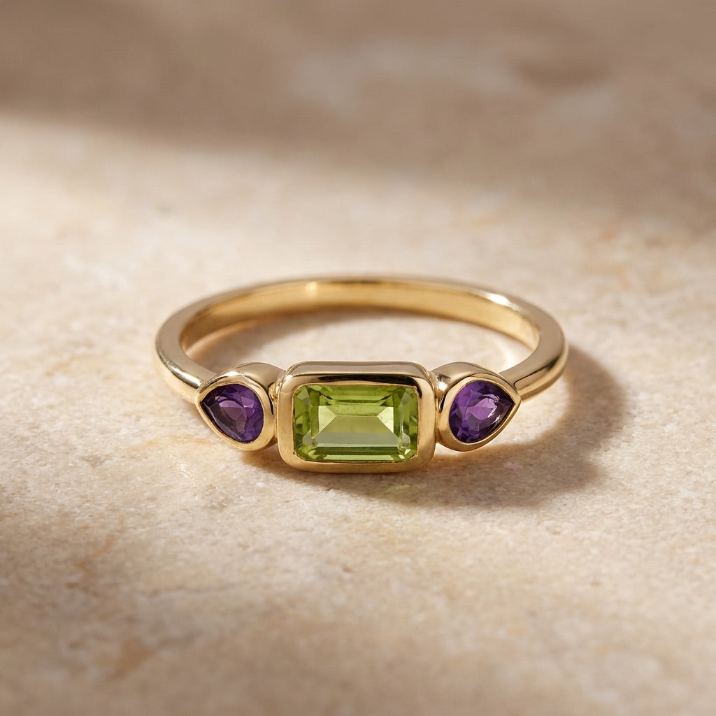 Gold ring with green and purple gemstones on a beige background