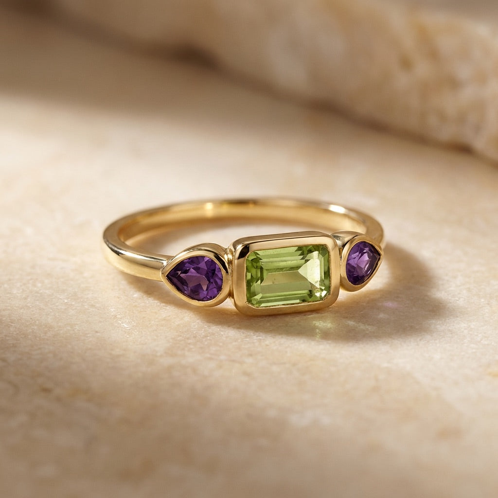 Gold ring with green and purple gemstones on a beige surface