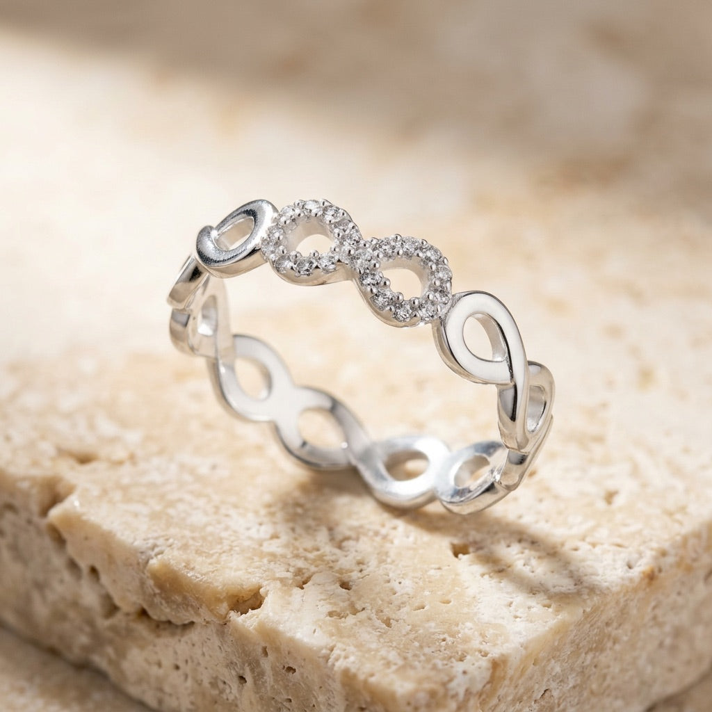 Silver ring with infinity symbol design on a beige stone surface