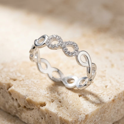 Silver ring with infinity symbol design on a beige stone surface