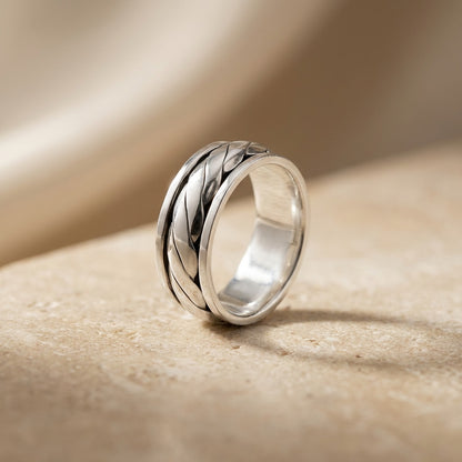 Silver ring with braided design on a beige surface