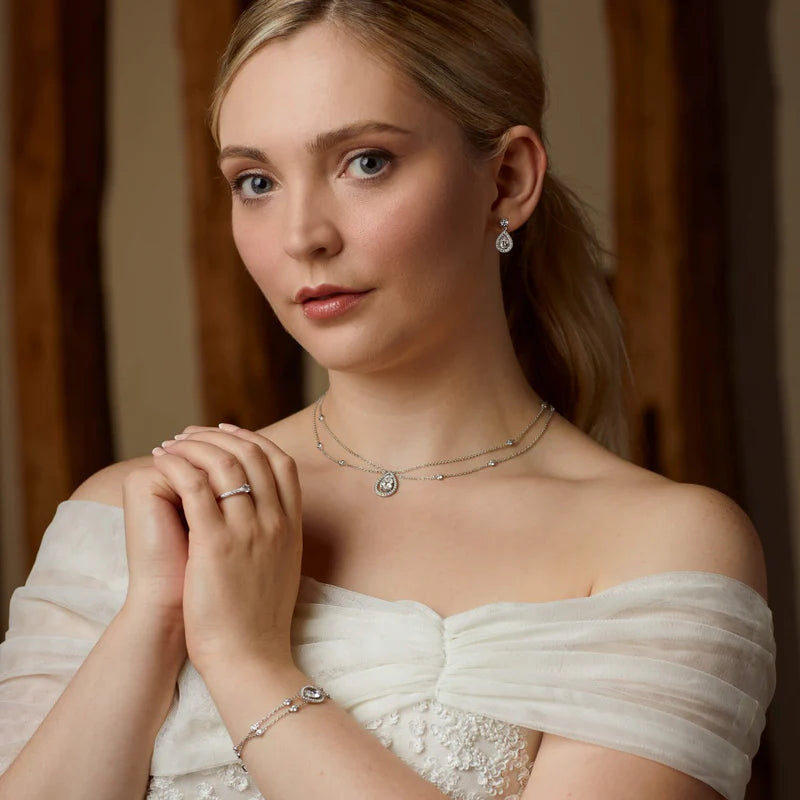 Woman wearing a white off-shoulder dress with jewellery, including a necklace, earrings, and bracelet.