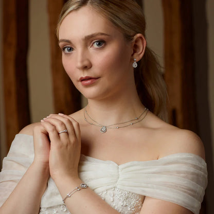 Woman wearing a white off-shoulder dress with jewellery, including a necklace, earrings, and bracelet.